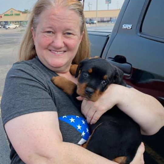 A woman holding a black and tan puppy with a blue collar featuring white stars