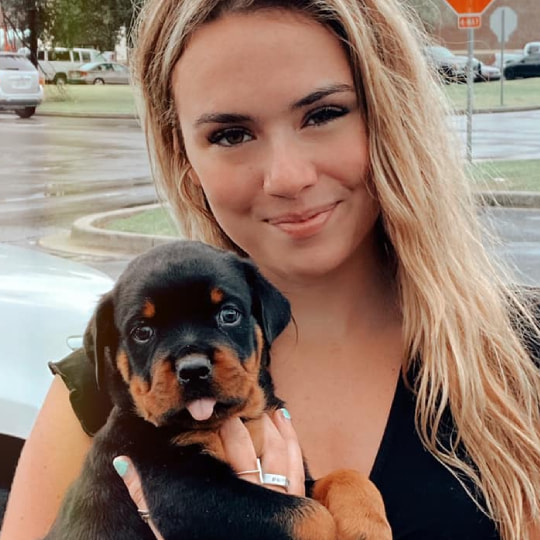 A woman holding a small black and tan Rottweiler puppy