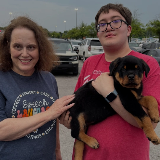 A mother and son standing in a parking lot and son holding a puppy