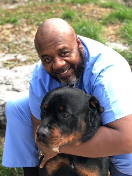 A man in blue scrubs hugs a large Rottweiler outdoors