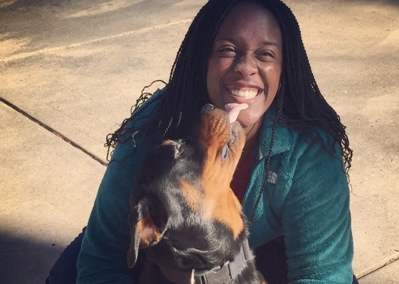 A woman smiles as a Rottweiler licks her face outside
